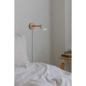 Umage Asteria bordlampe placeret som sengelampe, hvor dens integrerede LED giver et blidt og funktionelt lys.