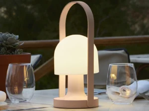 Marset Follow Me bordlampe på et udendørs spisebord en hyggelig aften, og spreder et varmt, blødt lys.