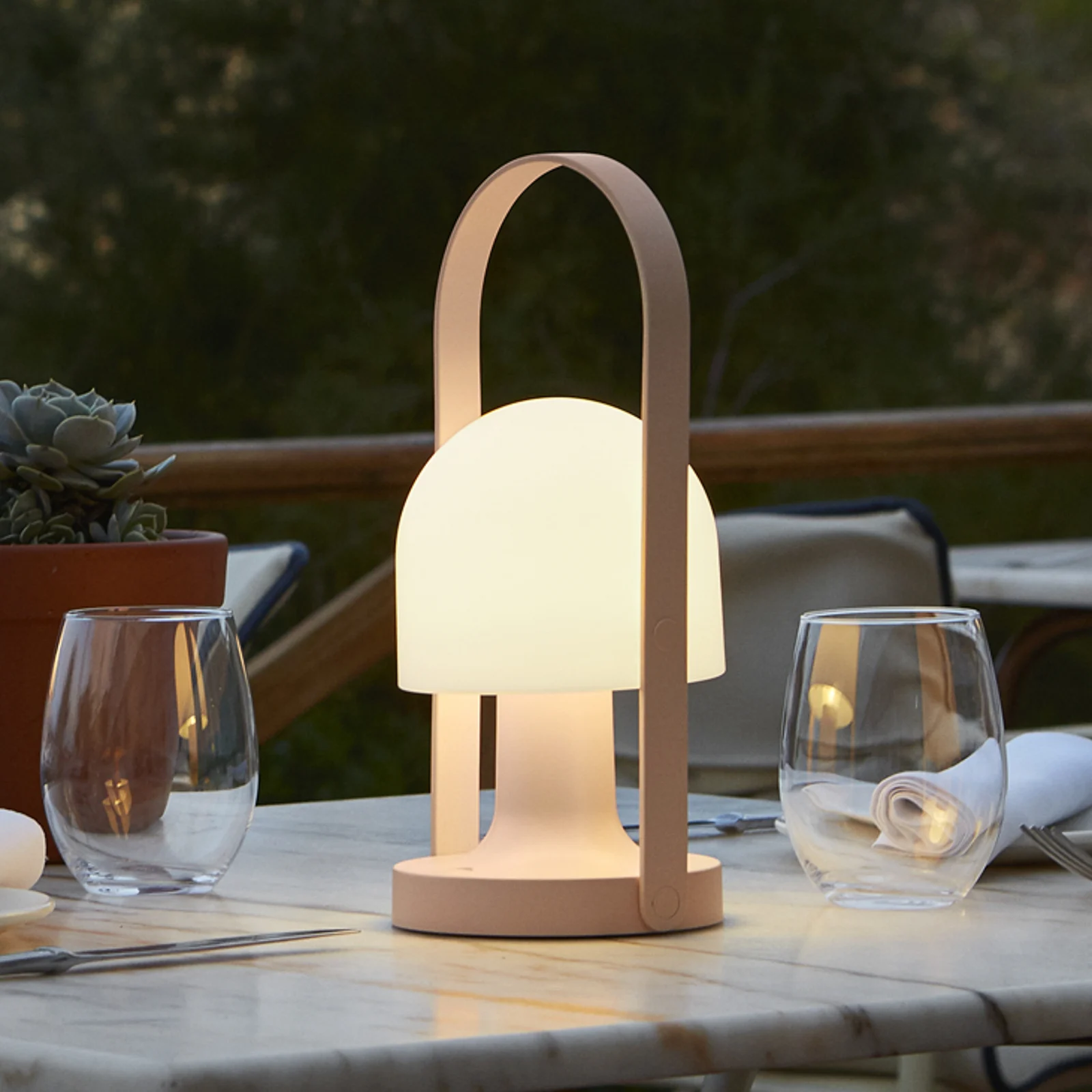 Marset Follow Me bordlampe på et udendørs spisebord en hyggelig aften, og spreder et varmt, blødt lys.